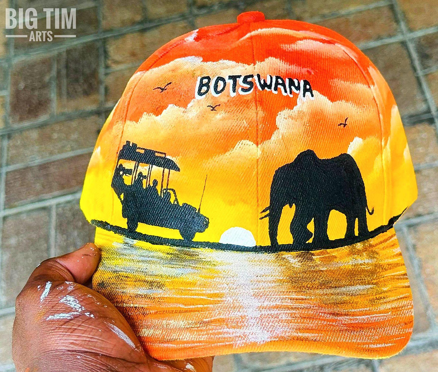 Elephant and vehicle silhouettes over orange sunset water on a cap.