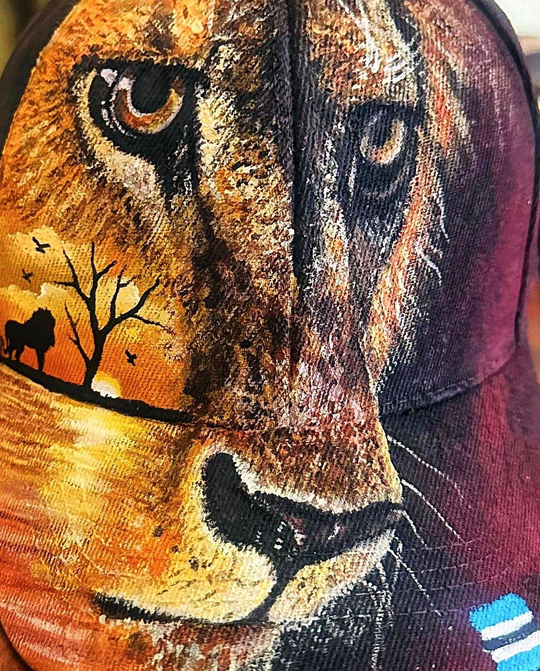 Lion face blended with a sunset and silhouetted tree on a cap.