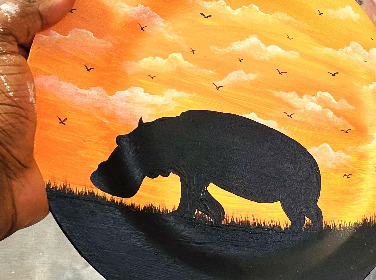 Hippopotamus silhouette beneath an orange sky dotted with birds.
