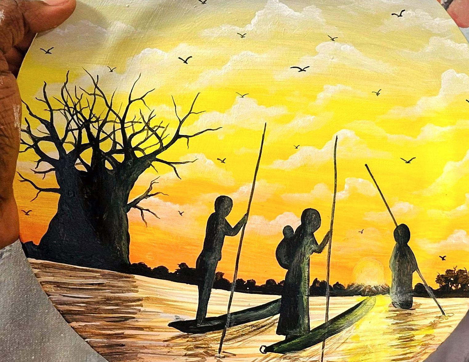Silhouetted figures with poles and narrow boats beside a large tree at sunset.