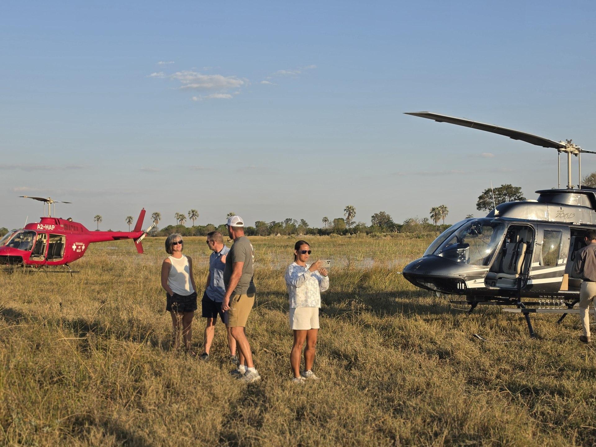 Guests talking between parked helicopters in evening light.